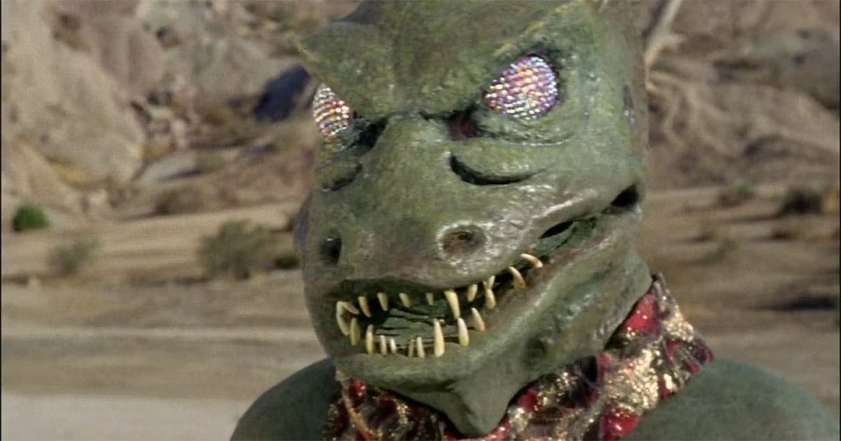 The Gorn Captain in "Arena," a large green-scaled reptilian alien with piercing yellow eyes, standing in a rocky landscape.