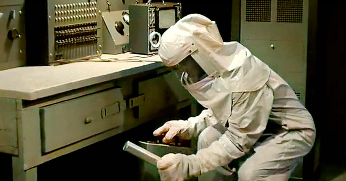 A scientist in a full-body protective suit and face shield crouches in a laboratory, carefully handling a metal canister.