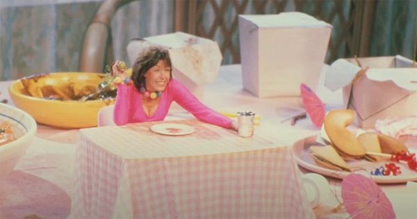 Lily Tomlin from the movie The Incredible Shrinking Woman sitting at a tiny table celebrating being small.